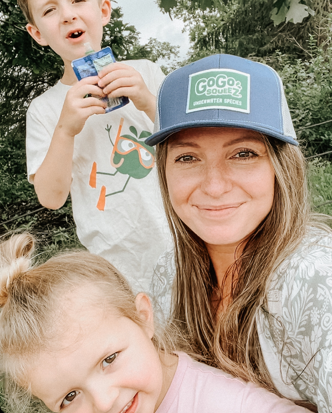 Gen Z mom walking in the park with two kids enjoying GoGo squeeZ applesauce pouches, representing modern parenting and consumer influence. Gen Z mom walking in the park with two kids enjoying GoGo squeeZ applesauce pouches, representing modern parenting and consumer influence.