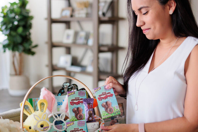 Alt text (featured image): Mom arranging an Easter basket filled with treats, toys, and chocolate Ring Pop candies on a table at home, illustrating how families curate personalized Easter baskets.